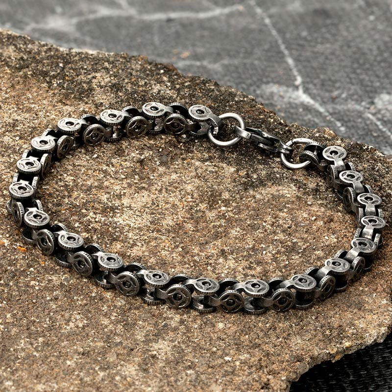 Men's punk style bracelet made of dark gray stainless steel with unique circular designs on a stone surface.
