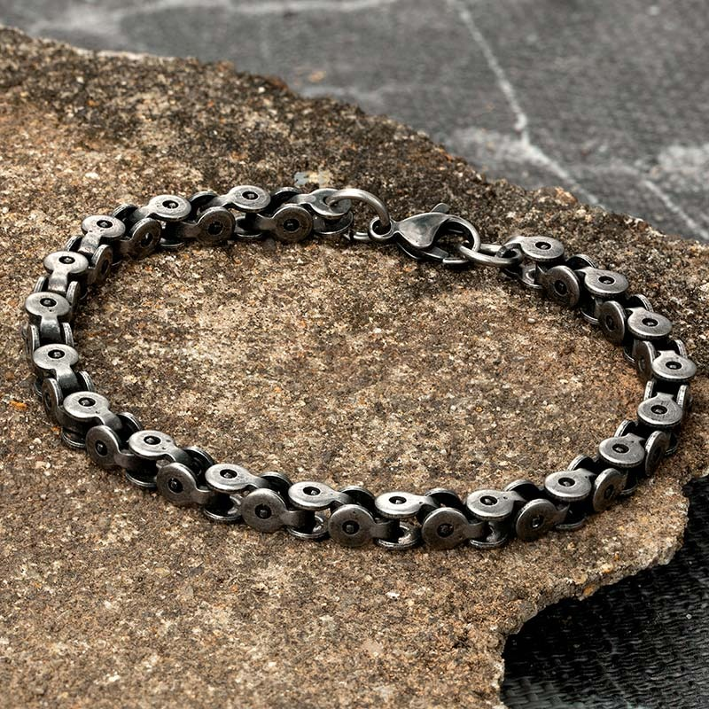 Men's punk style dark gray stainless steel bracelet displayed on textured rock surface.
