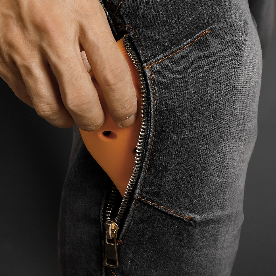 Close-up of a hand sliding a phone into the zipper pocket of men's slim biker jeans, showcasing functionality and style.