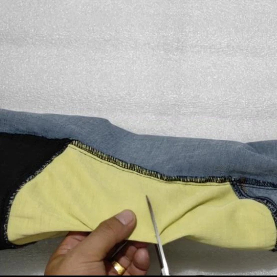 Cutting the protective lining of men's biker style jeans to enhance fit and style.