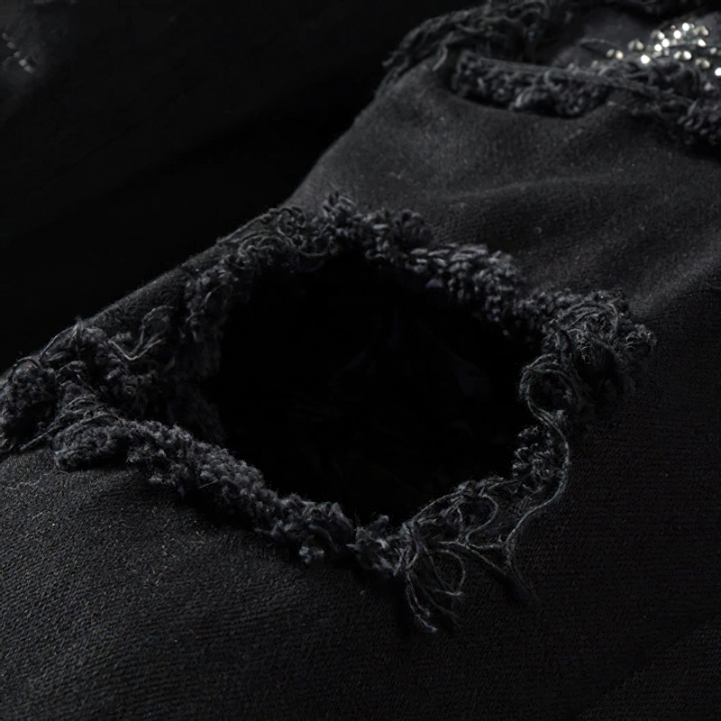 Close-up of ripped black denim jeans showcasing frayed edges and rhinestone detailing, perfect for punk fashion.