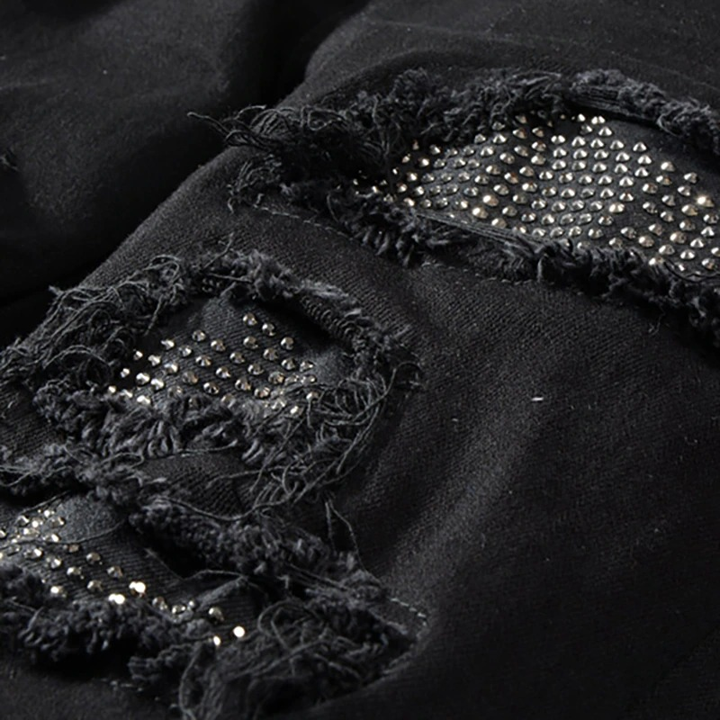 Close-up of black men's slim ripped jeans with rhinestone embellishments, showcasing stylish punk fashion details.