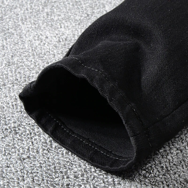 Close-up of the cuff of men's slim ripped jeans with rhinestones, showcasing black stretch denim and clean stitching.