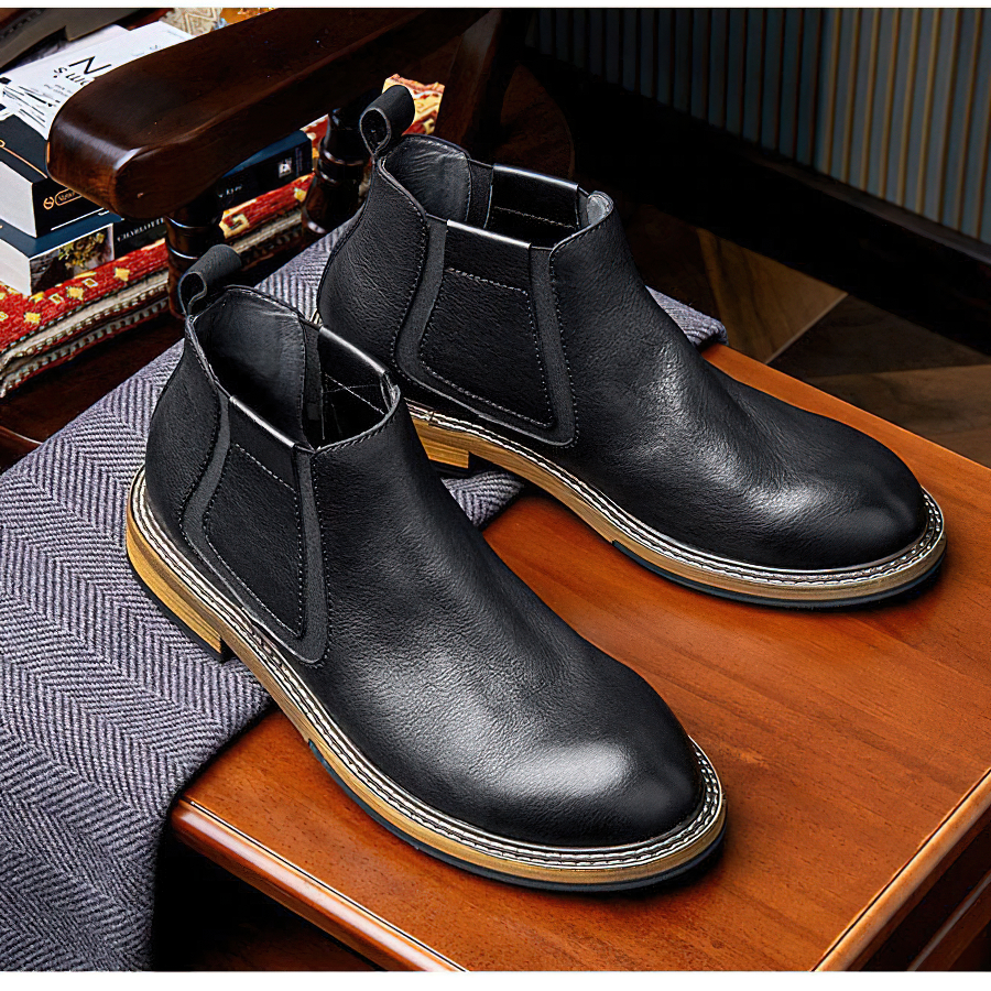 Men's black soft leather ankle boots with modern design on a wooden table.