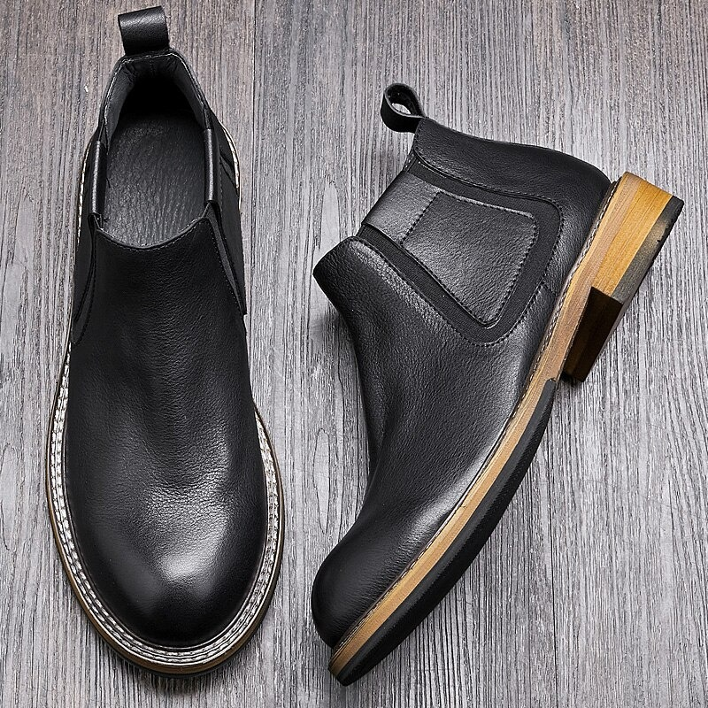 Men's black soft leather ankle boots with round toe and stylish wooden heel on wooden background.