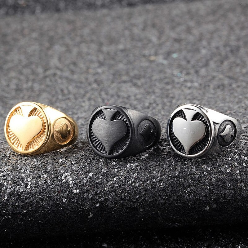 Men's heart signet rings in gold, black, and silver, showcasing a vintage rock style on a textured background.