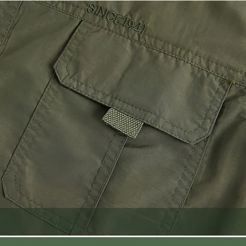 Close-up of olive green tactical shirt pocket featuring a flap and strap, showcasing durability and design.