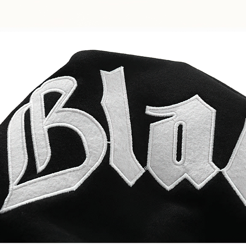 Close-up of black sweatshirt shoulder featuring stylish white embroidered letter patch detail.