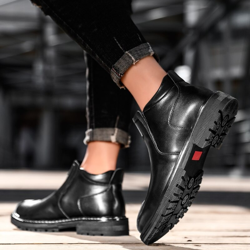 Men's black leather ankle boots displayed with casual jeans on a wooden surface.