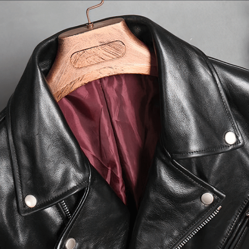Close-up of black waxed horsehide motorcycle jacket collar and cotton lining on wooden hanger.