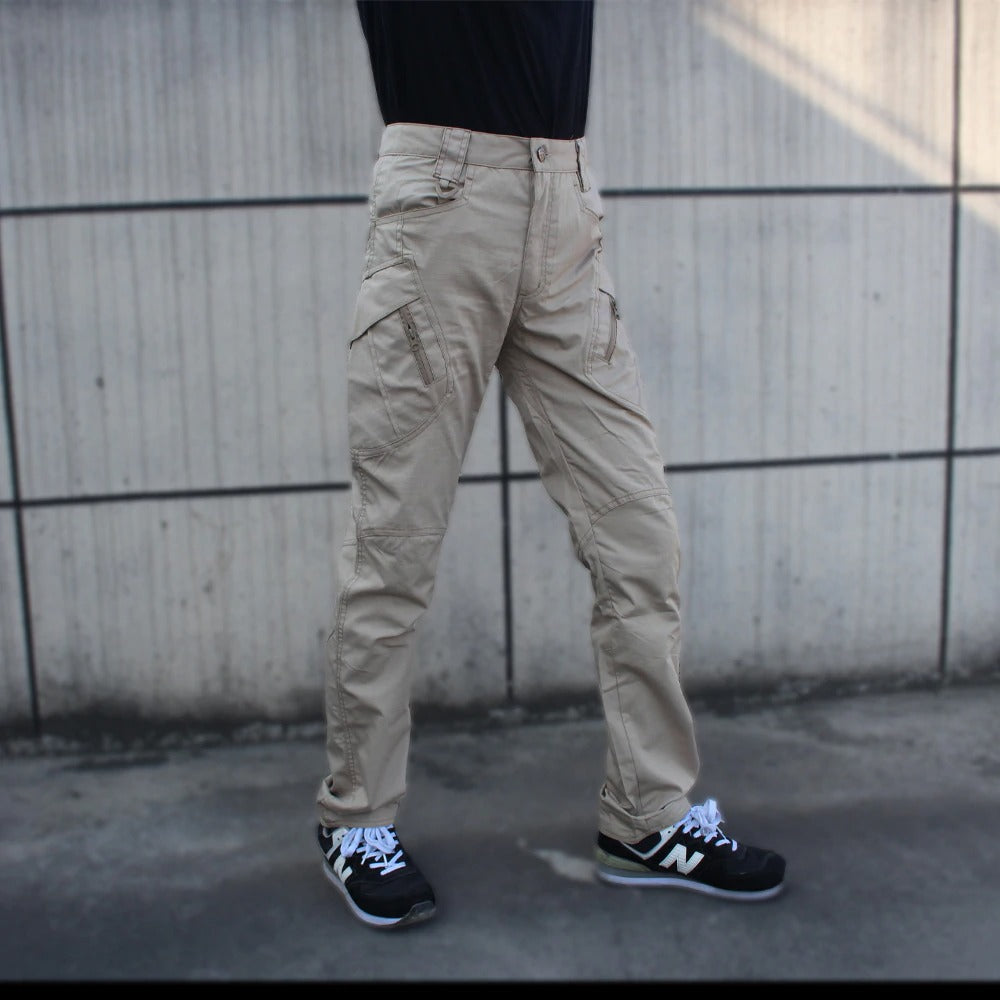Men's military tactical cargo pants in beige with multiple pockets, paired with New Balance shoes.