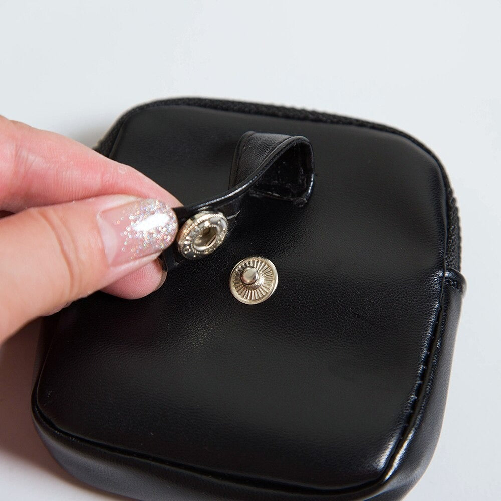 Close-up of a hand opening a black leather pouch with a snap button closure and decorative silver hardware.