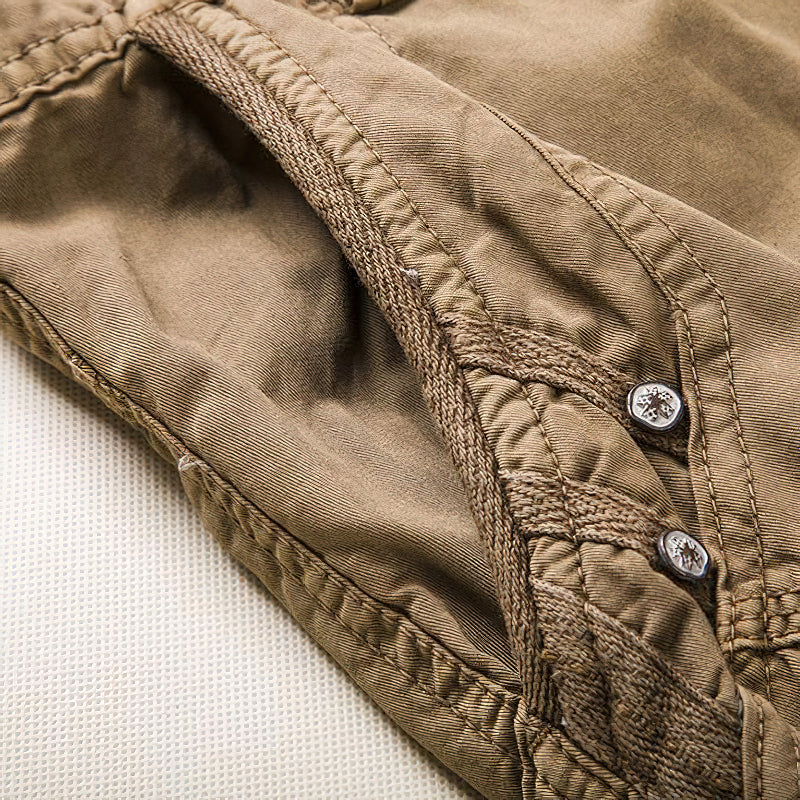 Close-up of the button and seam detail on men's multi-pocket cargo shorts in khaki fabric.
