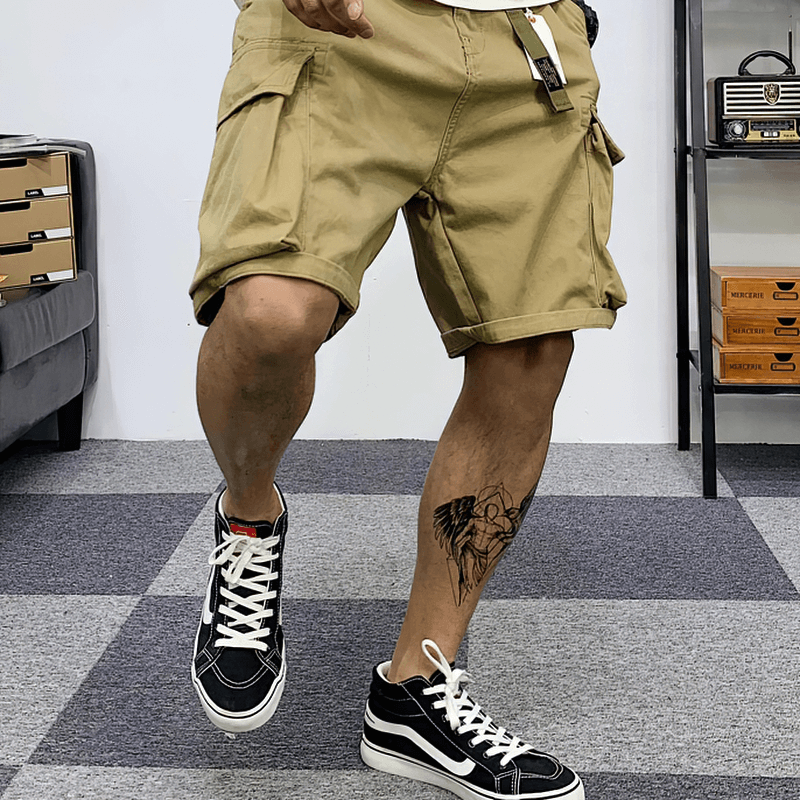 Man wearing multi-pocket military cargo shorts in beige with stylish sneakers, showcasing alternative male fashion.