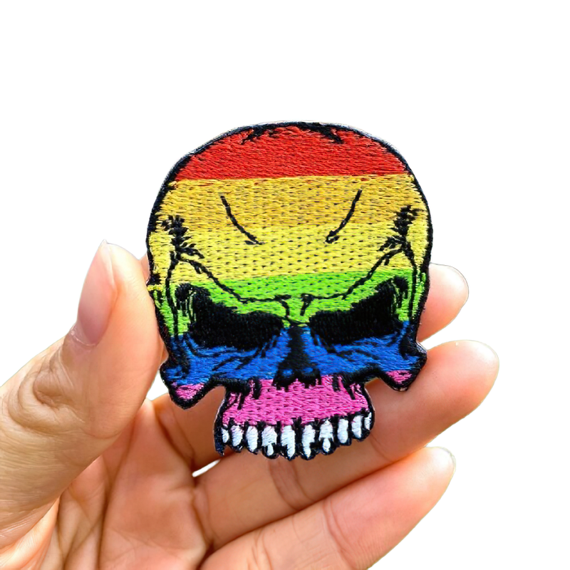 Hand holding a vibrant multicolored skull iron-on patch, perfect for adding trendy flair to jackets and clothes.