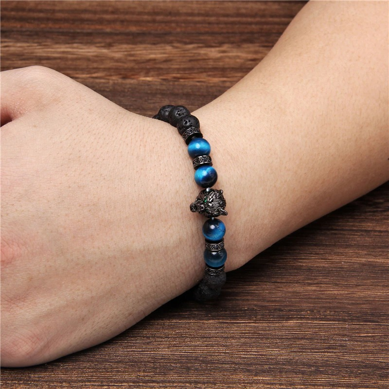 Natural black lava stone bracelet with wolf charm and blue beads on a wrist, showcasing alternative jewelry style.