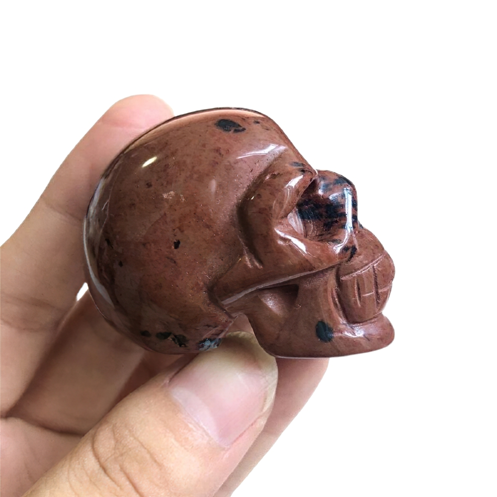 Handholding a natural crystal skull for home decoration, featuring earthy red hues and detailed carving.