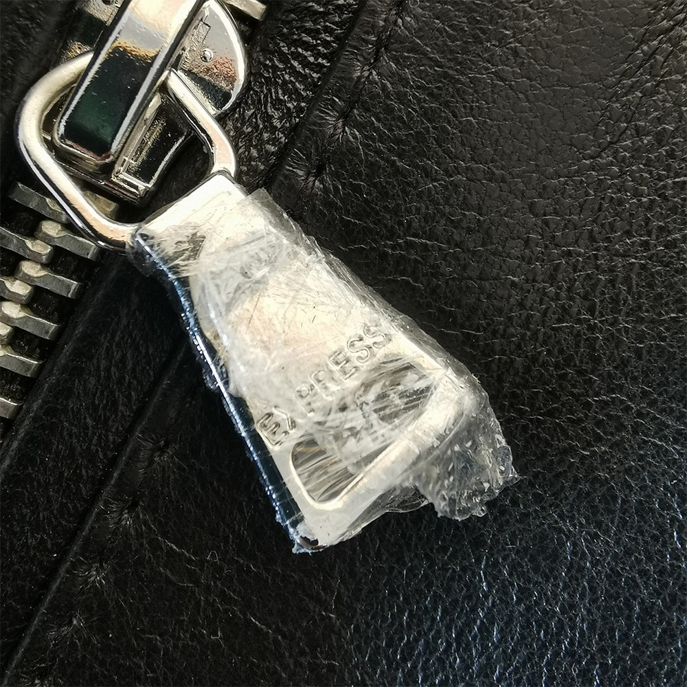 Close-up of a silver zipper with protective plastic on a black sheepskin leather jacket.