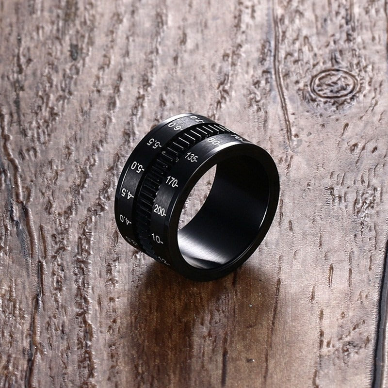 Stainless steel black camera lens ring on wood surface, perfect alternative jewelry for photographers.