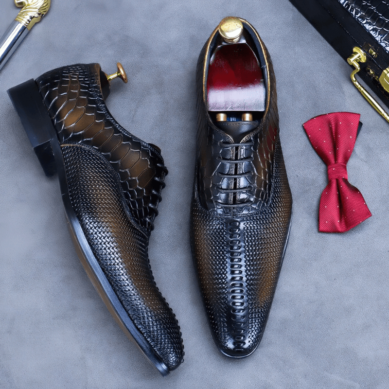 Stylish black leather Oxford shoes with unique texture, paired with a red bow tie for a fashionable look.
