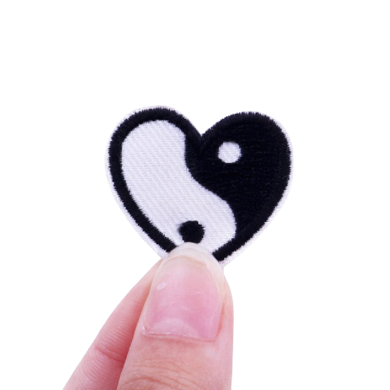 Heart-shaped Yin Yang patch held between fingers, perfect for customizing clothing with a stylish flair.