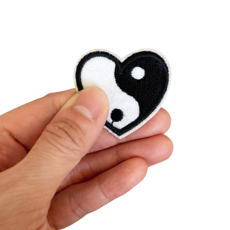 Hand holding a Yin Yang heart-shaped patch, perfect as a stylish unisex clothing accessory.