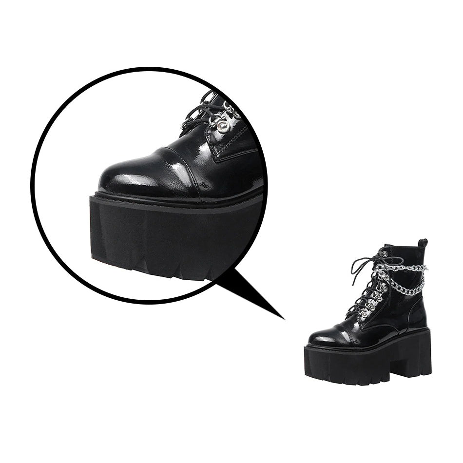 Close-up of black patent leather gothic platform boots with laces and metal chain detail.