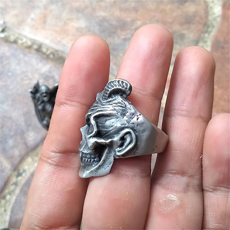 Close-up of a stainless steel plague devil skull ring held between fingers, perfect for rock and goth fashion.