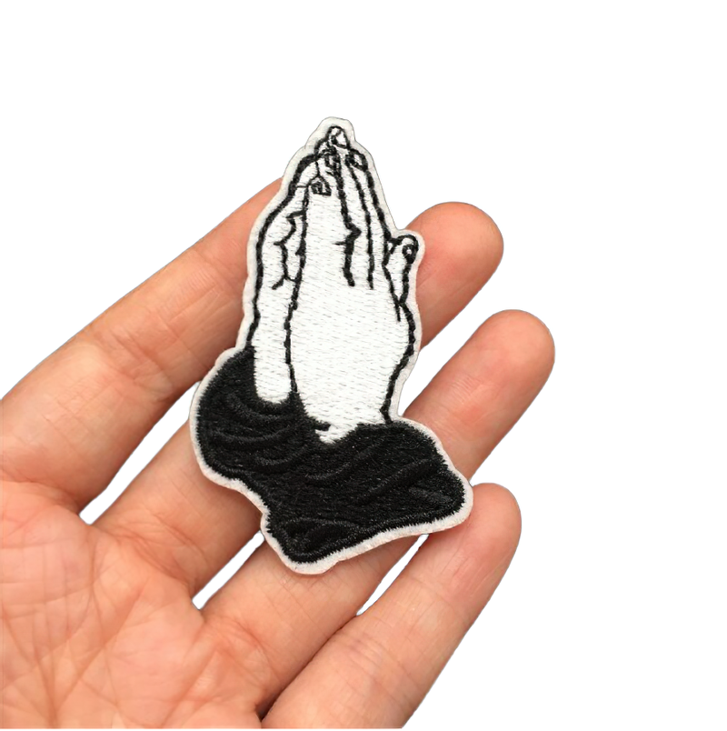 Detailed praying hands patch in hand; stylish embroidered accessory for clothing, ideal for unisex fashion.