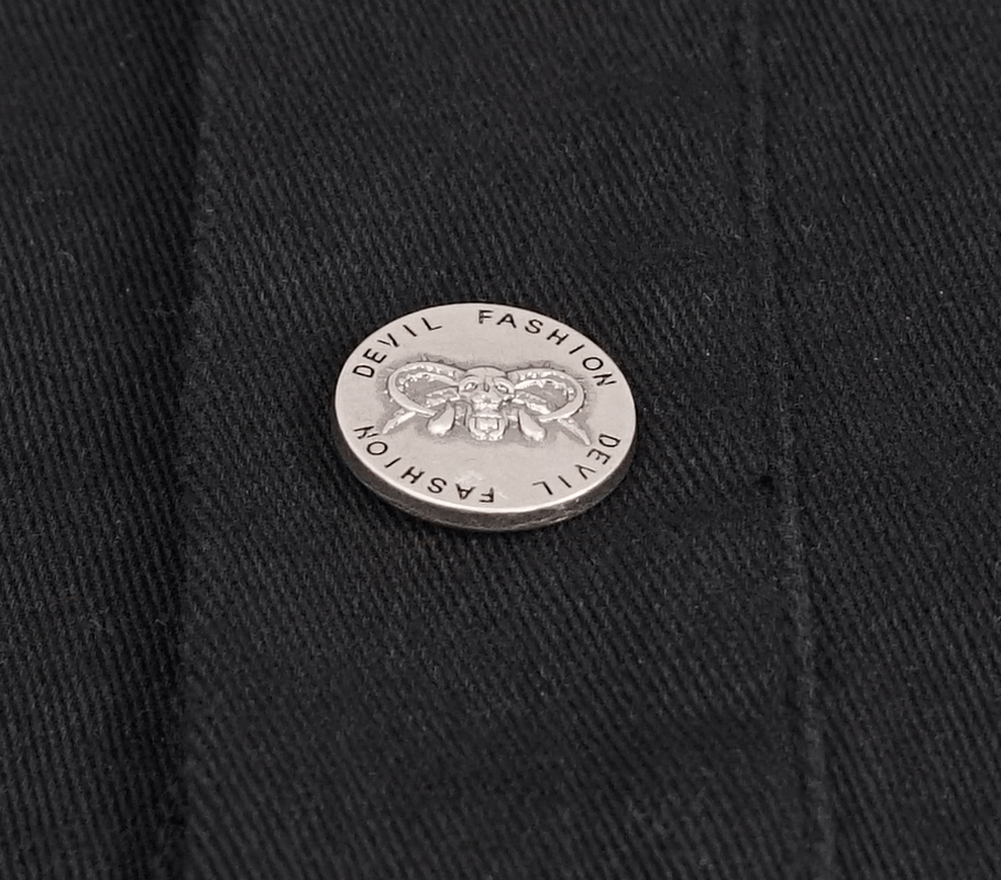Close-up of a silver decorative button on a black punk vest, featuring a skull and ram design.