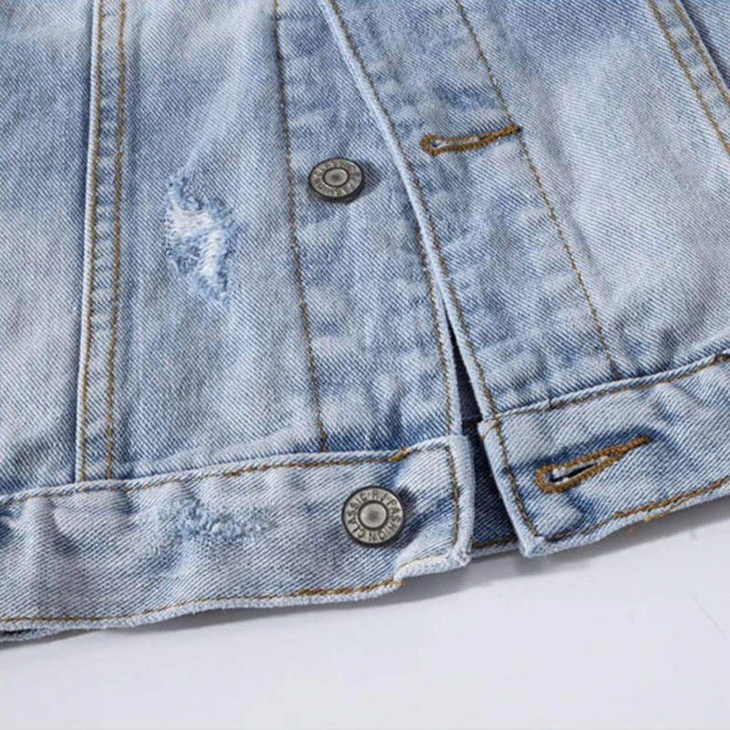 Close-up of a blue faded denim vest showcasing stylish ripped details and metal buttons for a punk rock look.