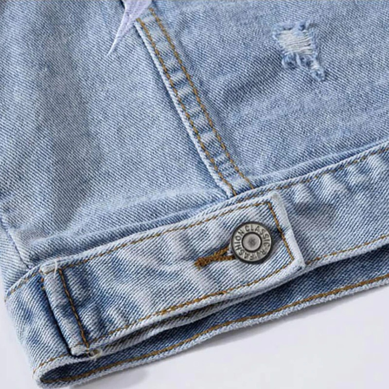 Close-up of a punk men's ripped denim vest with cool patches and a faded blue finish, showcasing unique style details.