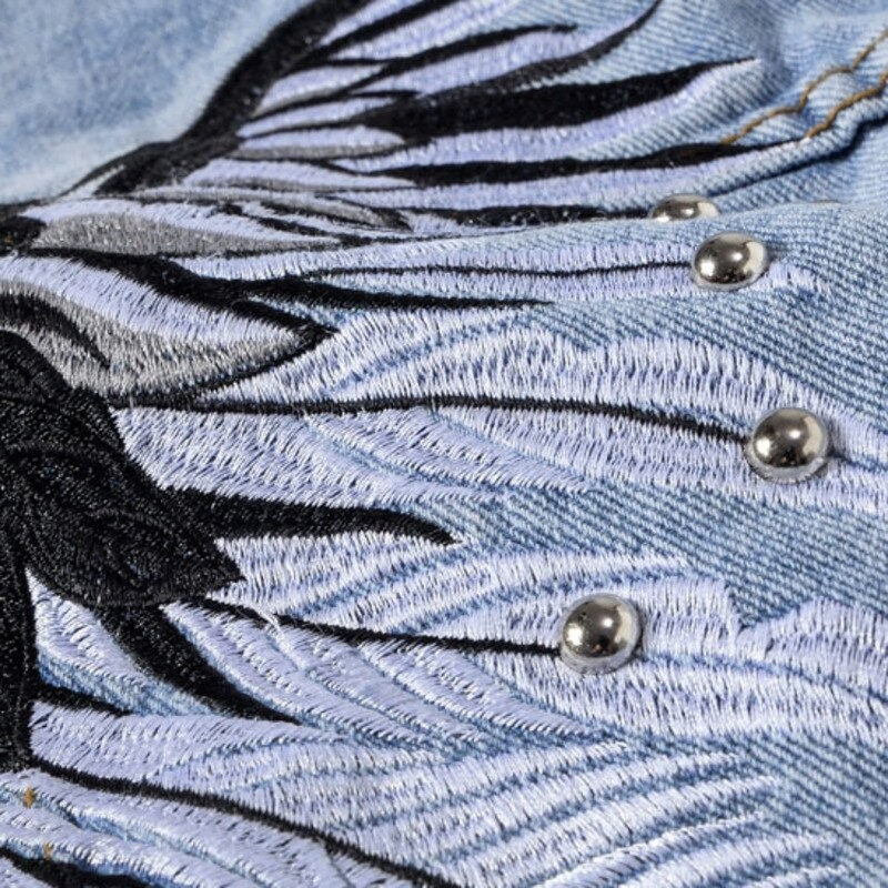 Close-up of punk denim vest with intricate blue rock style embroidery and shiny studs.