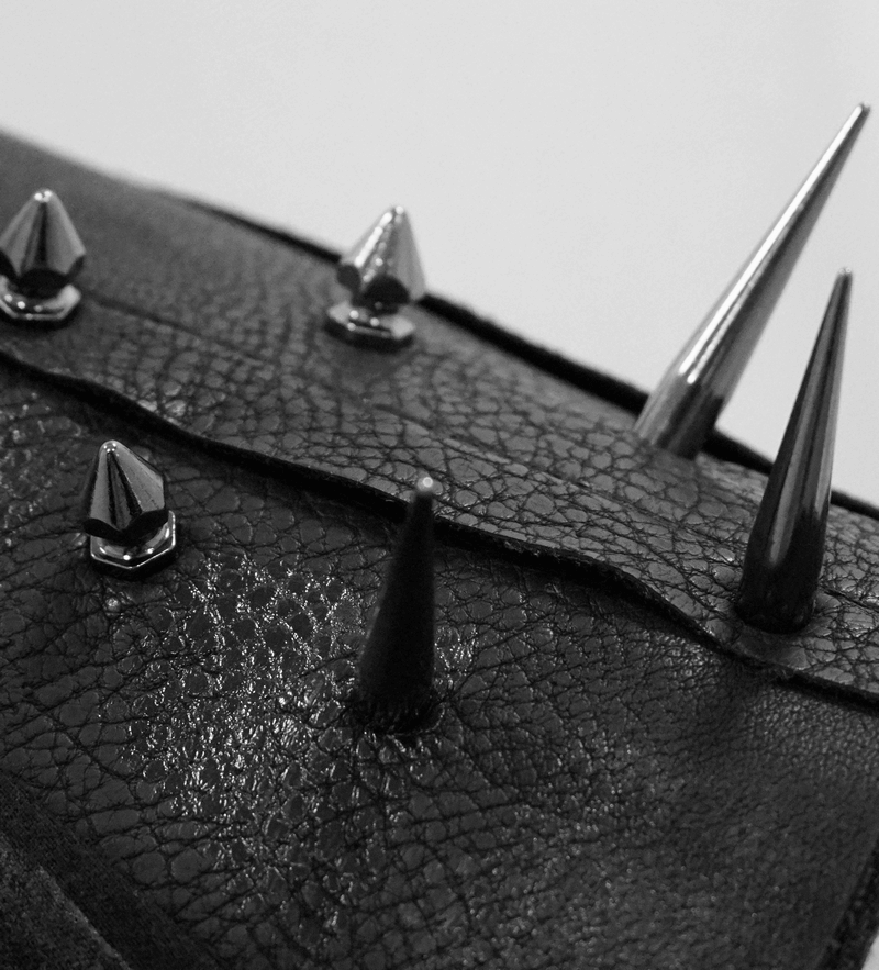 Close-up of black leather with shiny spikes and rivets, showcasing punk fashion style and edgy details.