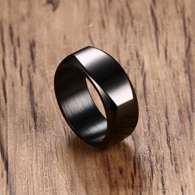 Sleek black stainless steel ring on a wooden surface, perfect for unisex fashion or a modern wedding band.