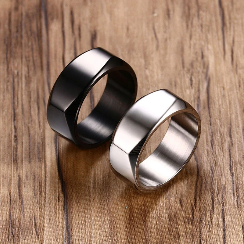 Two punk stainless steel rings, one black and one silver, stylish unisex wedding bands on a wooden background.