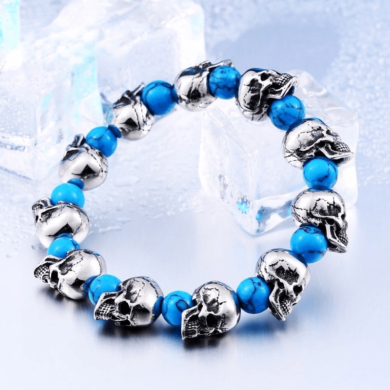 Punk style elastic wristband with silver skull head beads and blue accent beads against a cool backdrop.
