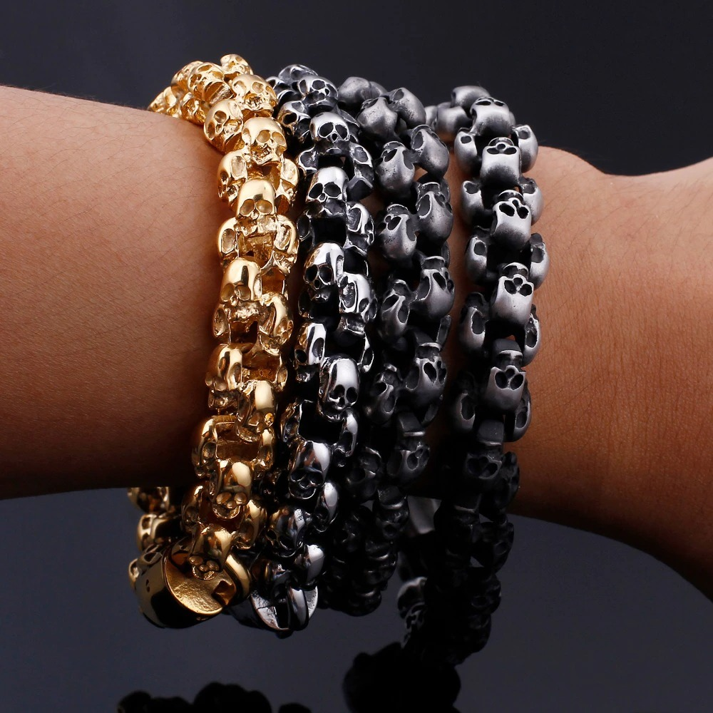 Stylish punk skull bracelets in gold and black stainless steel on a wrist, showcasing edgy men's jewelry.
