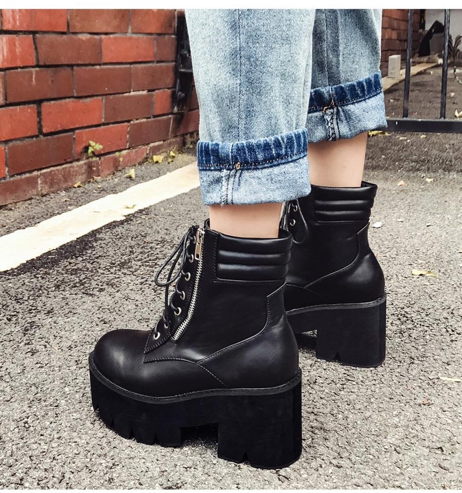 Women's black platform ankle boots with laces and zipper, styled with rolled-up jeans in a street setting.
