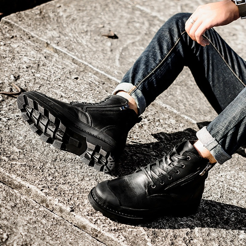 Men's rock style ankle boots in black leather, featuring laces and chunky soles, paired with denim jeans for a stylish look.
