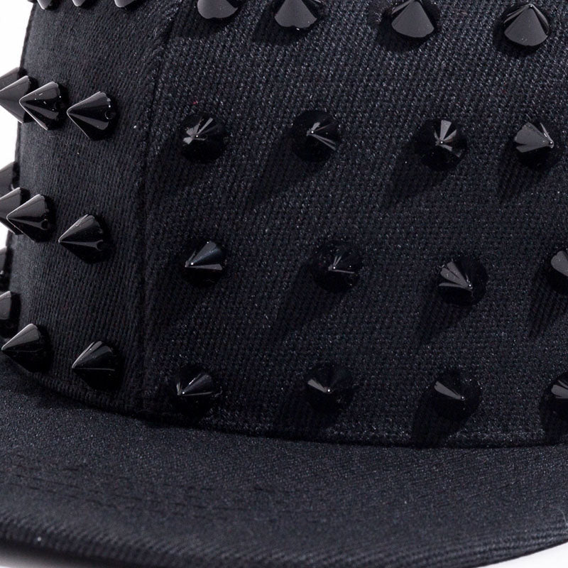 Close-up of a black spiked snapback cap featuring prominent black spikes, perfect for punk and rock fashion.