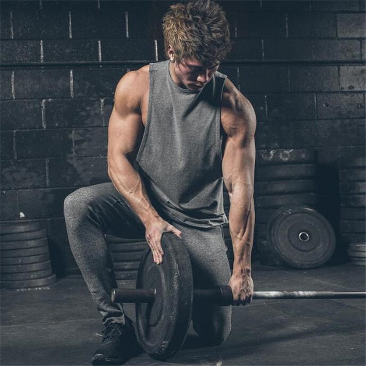 Muscular man wearing a sleeveless rock-style tank top lifting a weight in a gym setting.