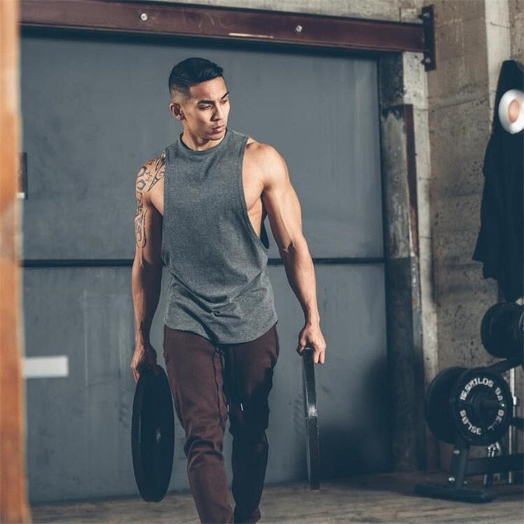 Muscular man in a sleeveless rock style tank top lifting weights at the gym, showcasing fitness and alternative fashion.