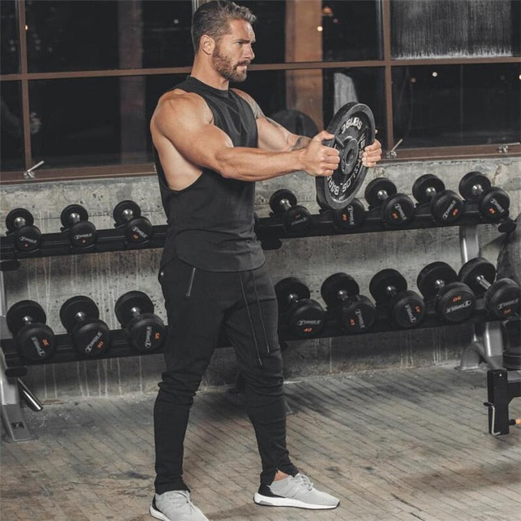 Muscular man in sleeveless black tank top lifting weights in gym, showcasing rock style fitness clothing.