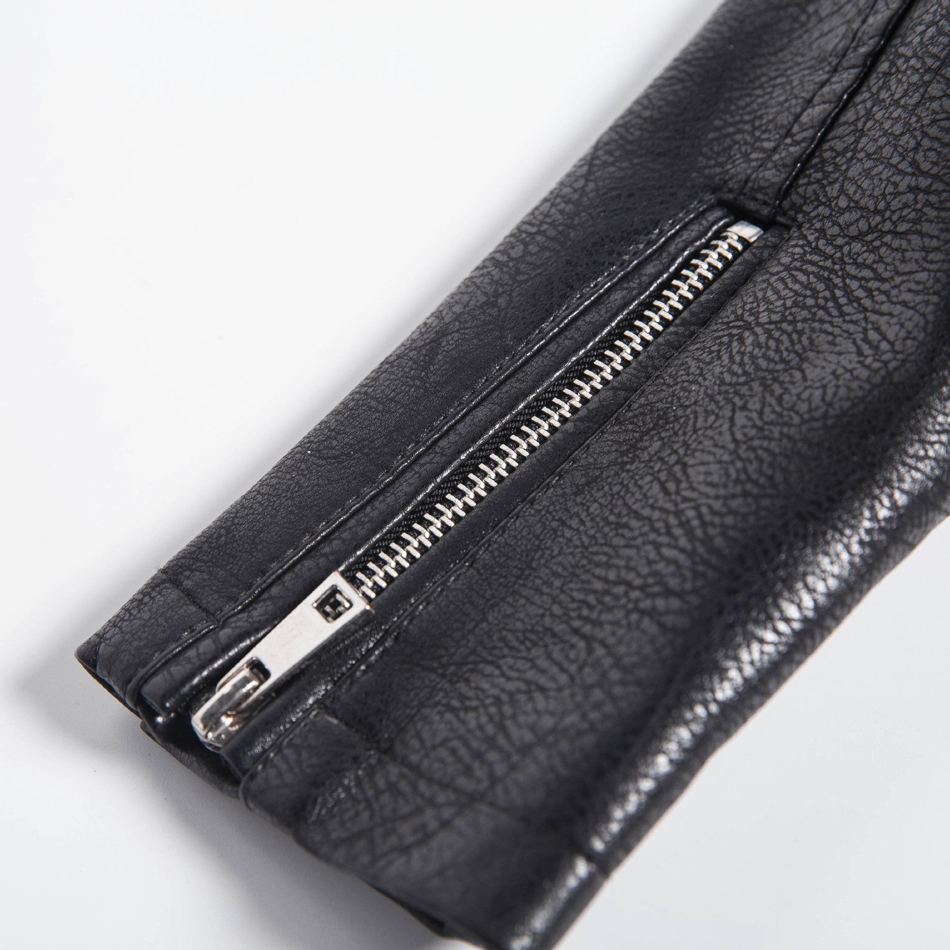 Close-up of black faux leather motorcycle jacket sleeve with silver zipper detailing for a rocker chic look.