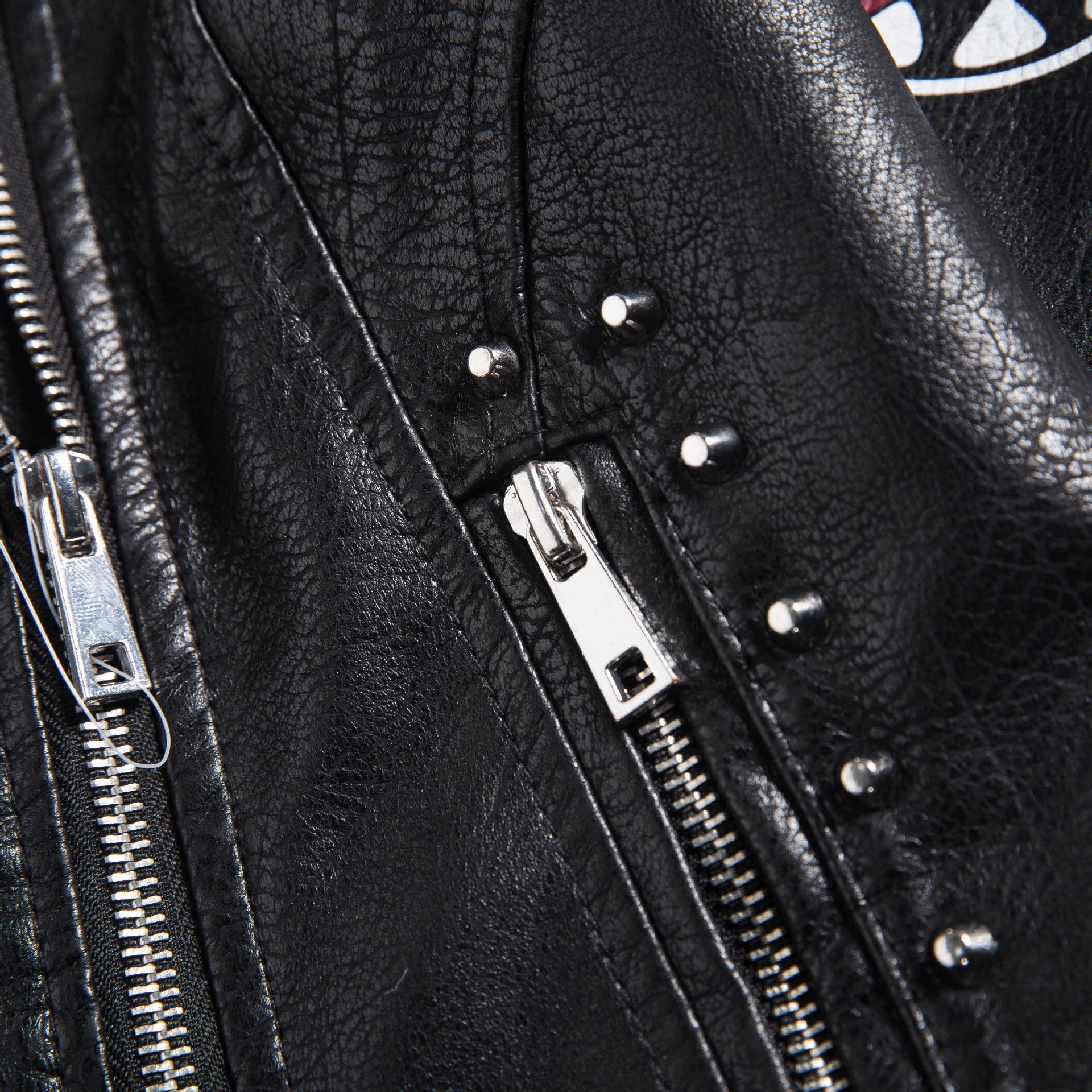 Close-up of zippers and studs on a women's faux leather motorcycle jacket, showcasing rock style details.