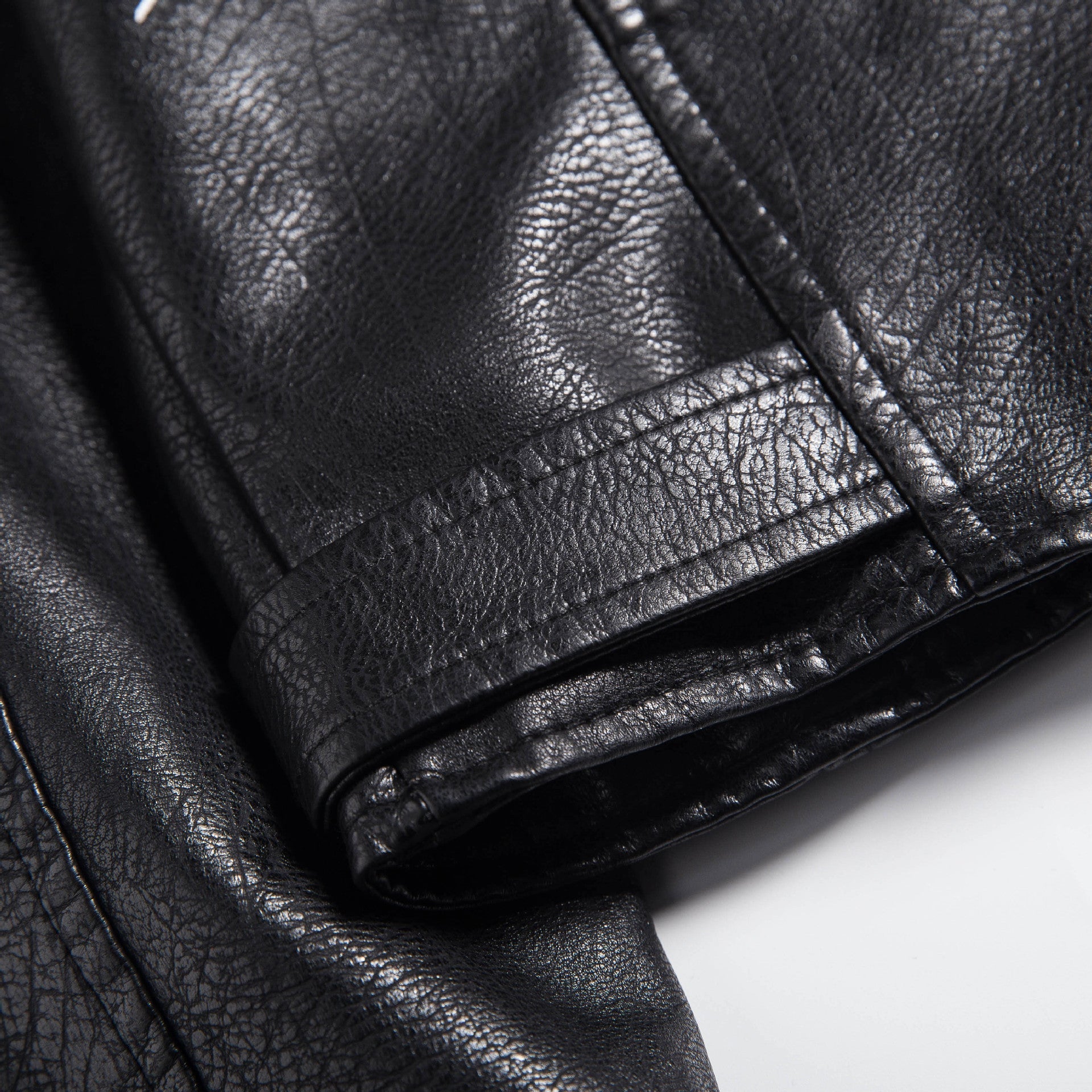 Close-up of a luxurious faux leather motorcycle jacket showcasing its textured black fabric and stylish cuff design.
