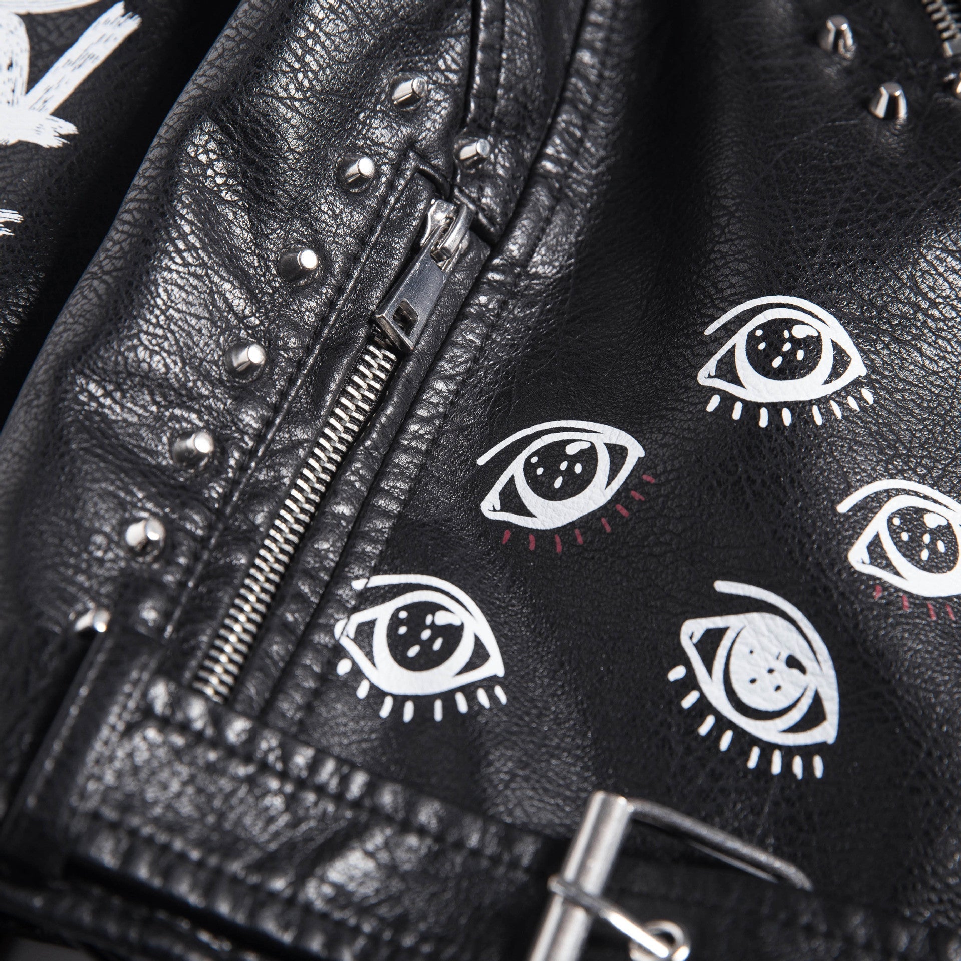 Close-up of a women's faux leather motorcycle jacket featuring 3D eye prints and metal studs, perfect for rocker styles.