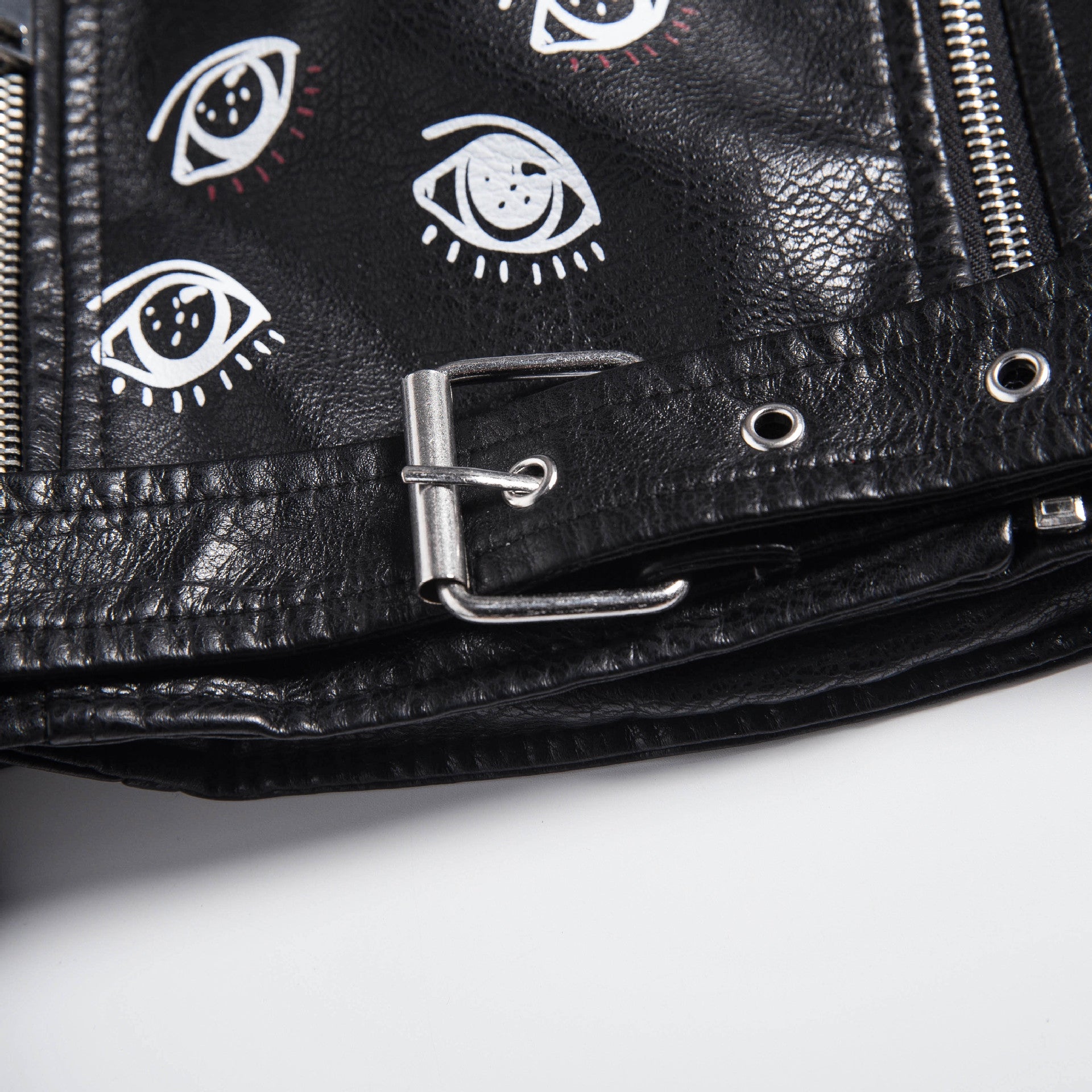 Close-up of a black faux leather motorcycle jacket featuring eye prints and silver zippers for a rock-inspired look.