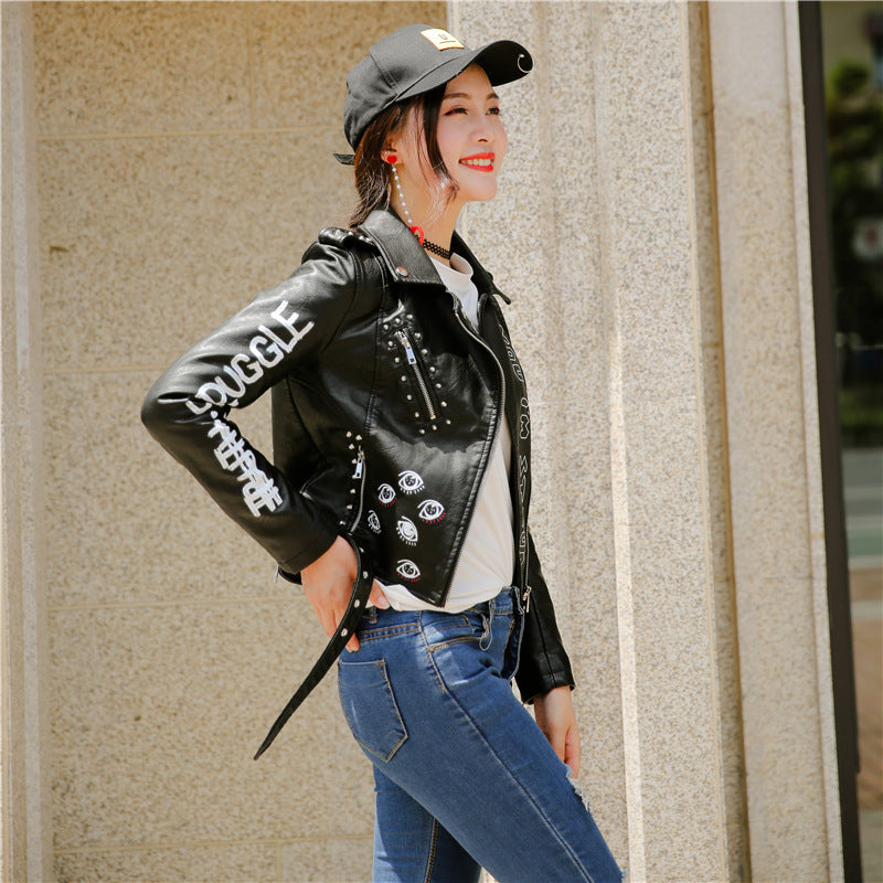 Stylish woman in a faux leather motorcycle jacket with studs, enjoying a sunny day, paired with jeans and a cap.